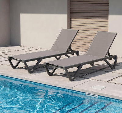 Two grey aluminum sling chaise loungers poolside on a patio deck